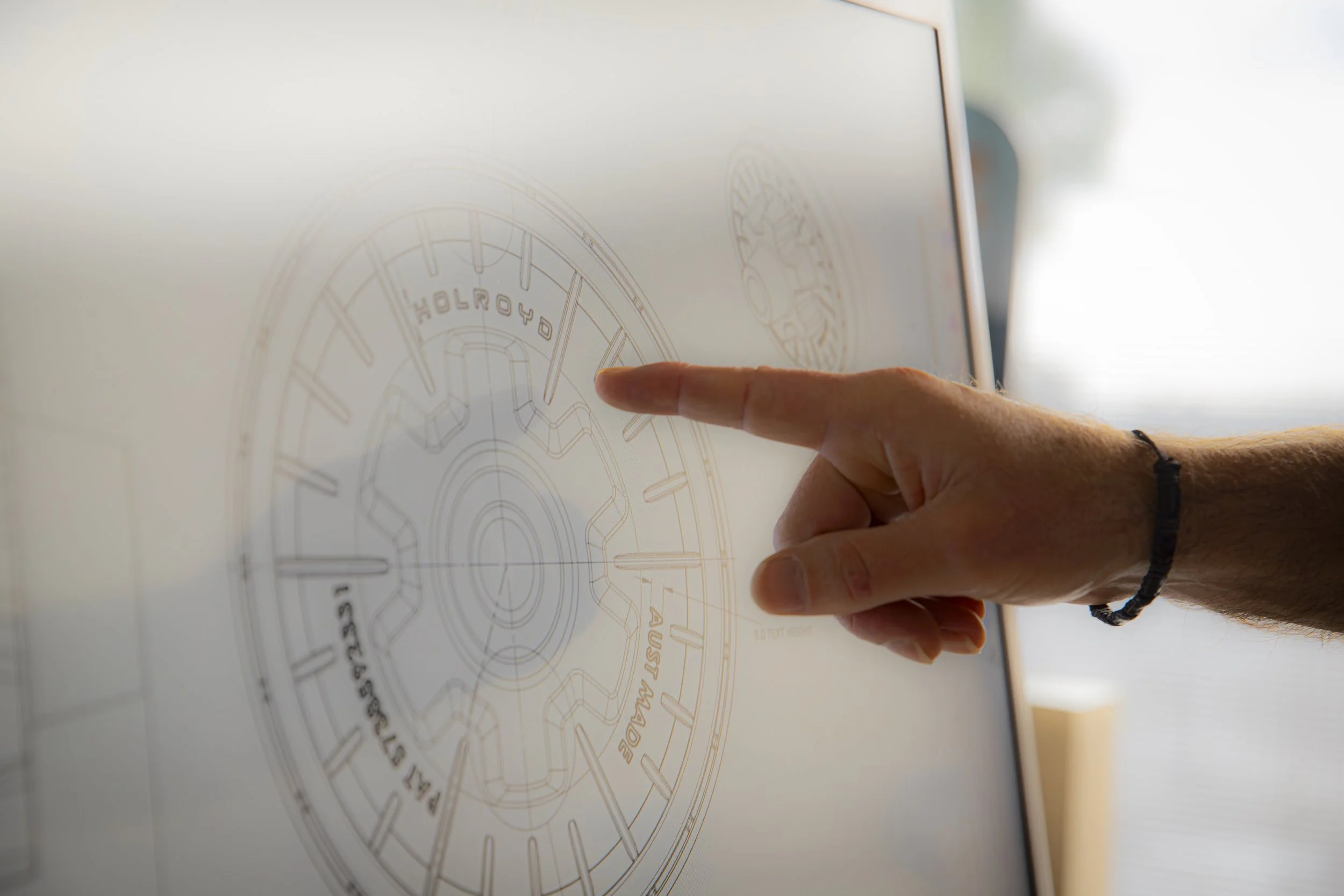 A person's hand pointing at a technical blueprint or schematic diagram displayed on a screen.
