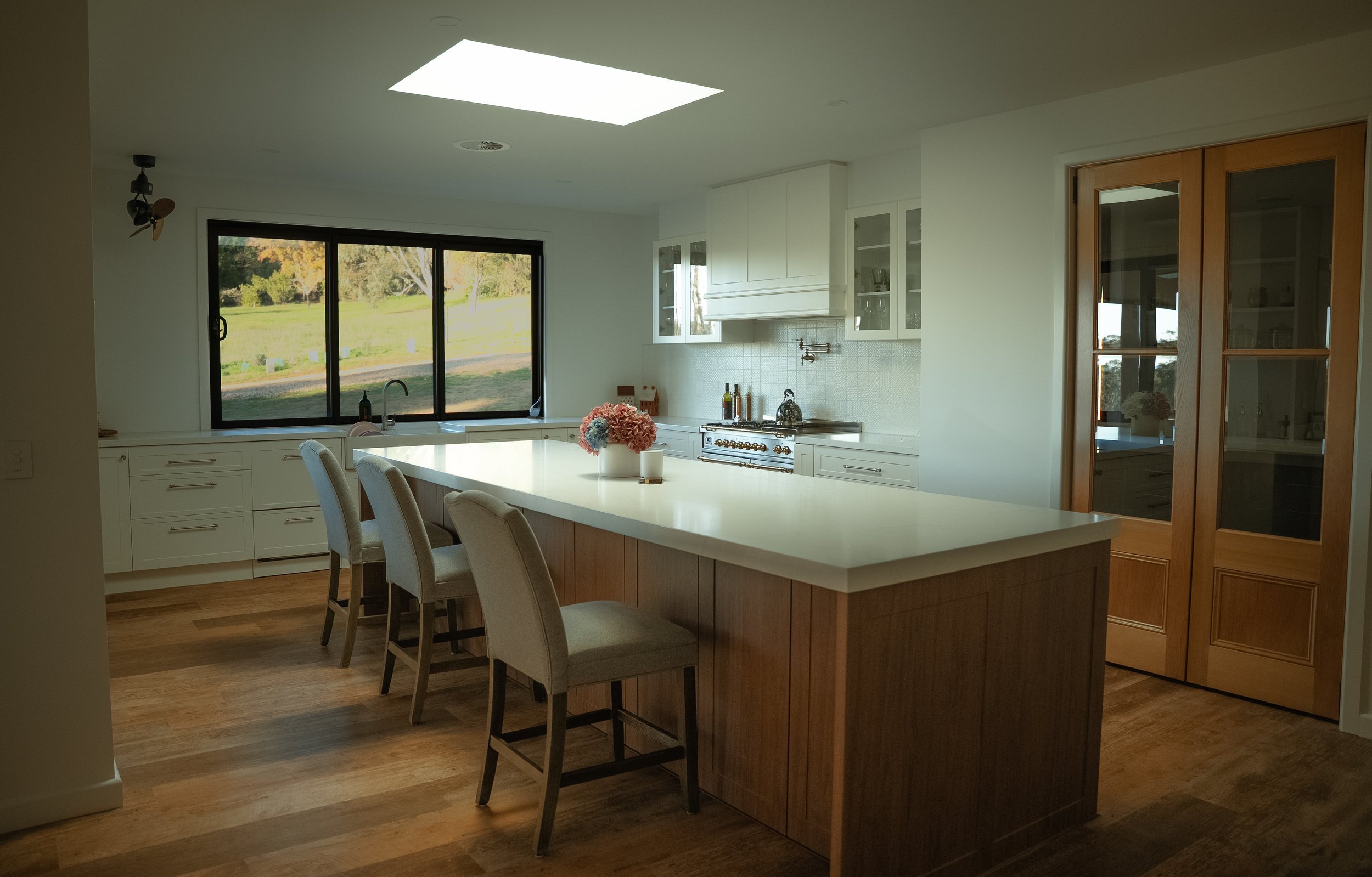 Bright kitchen with large window, white cabinets, kitchen island with seating, wooden floors, and a skylight.