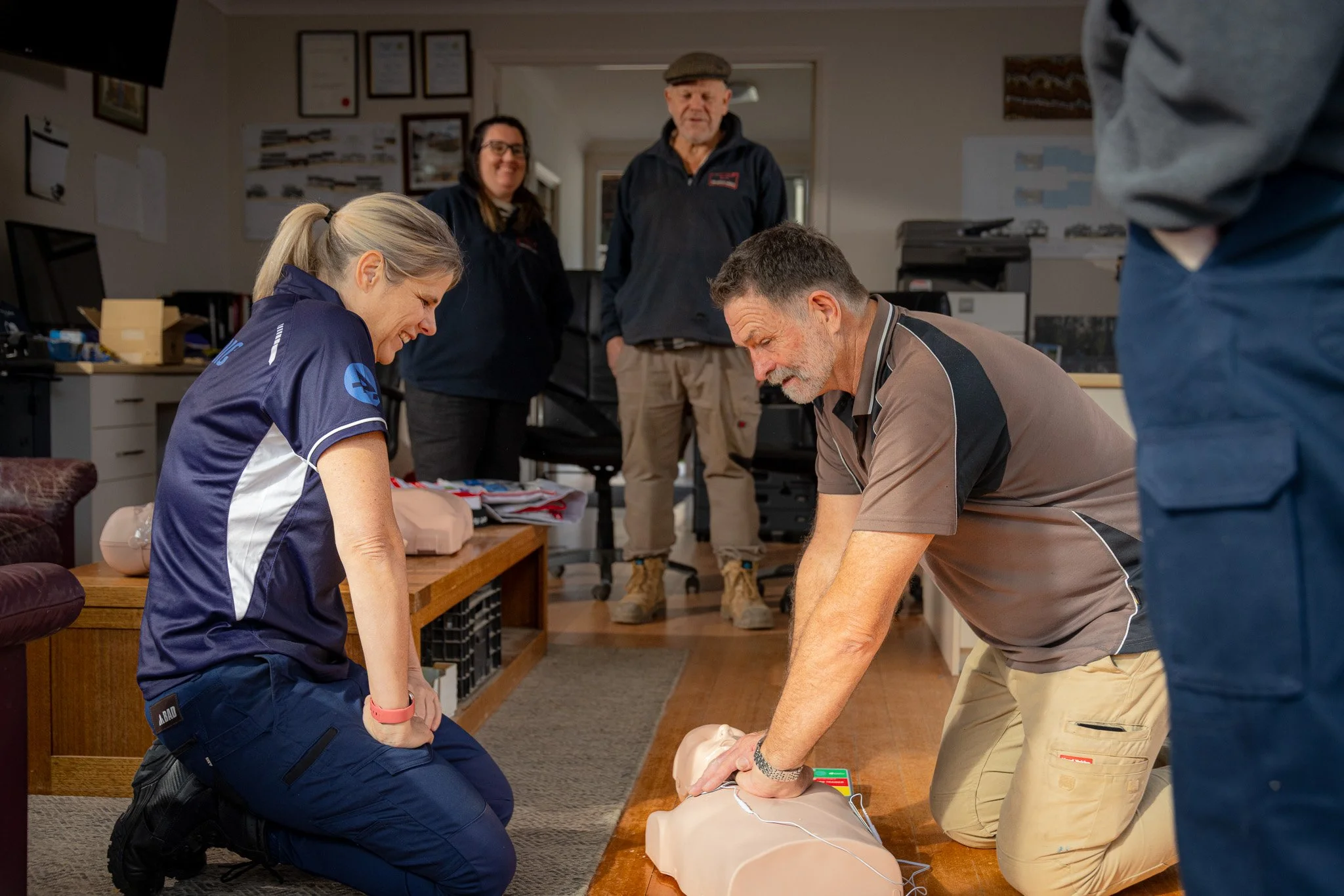 People participating in a CPR training session, practicing on a CPR manikin in an indoor classroom setting.