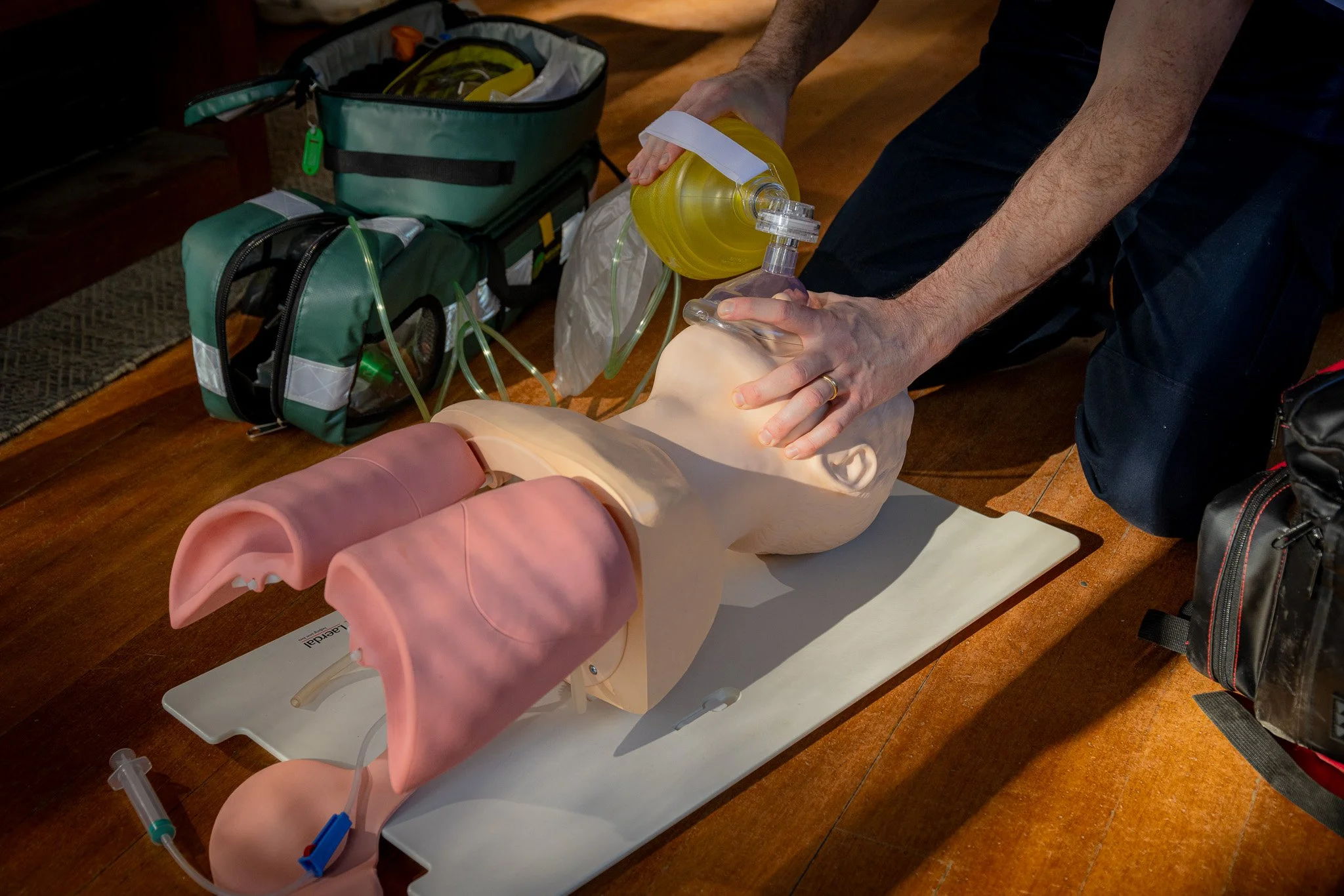 Person practicing CPR on a medical training mannequin with a mask, tubes, and an oxygen tank nearby.