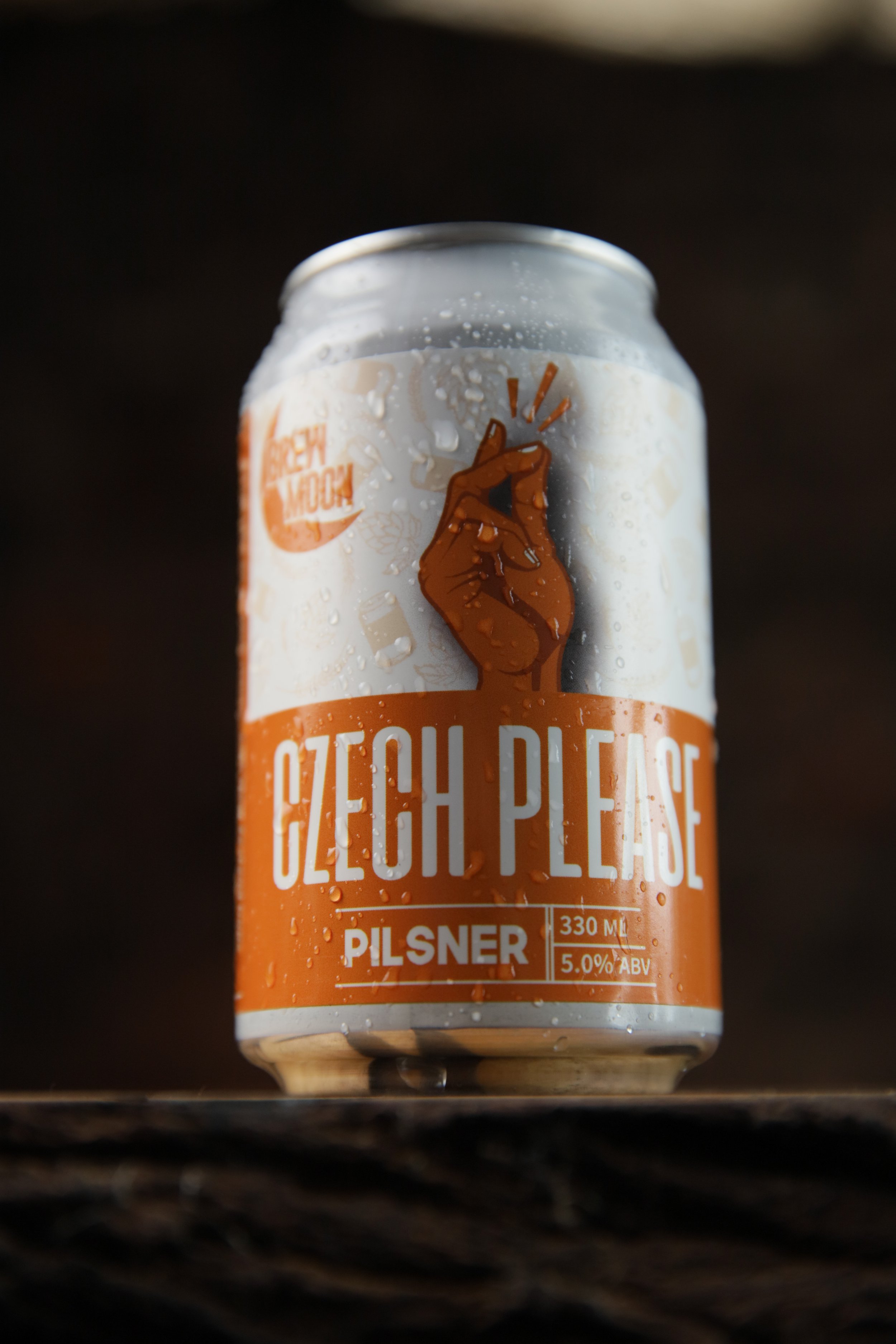 A can of Czech Please Pilsner beer with condensation on the outside, placed on a wooden surface.