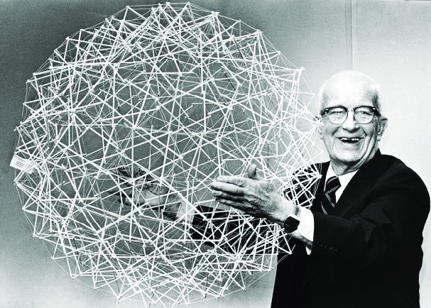 J. Buckminster Fuller holding up a geodesic tensegrity sphere smiling.