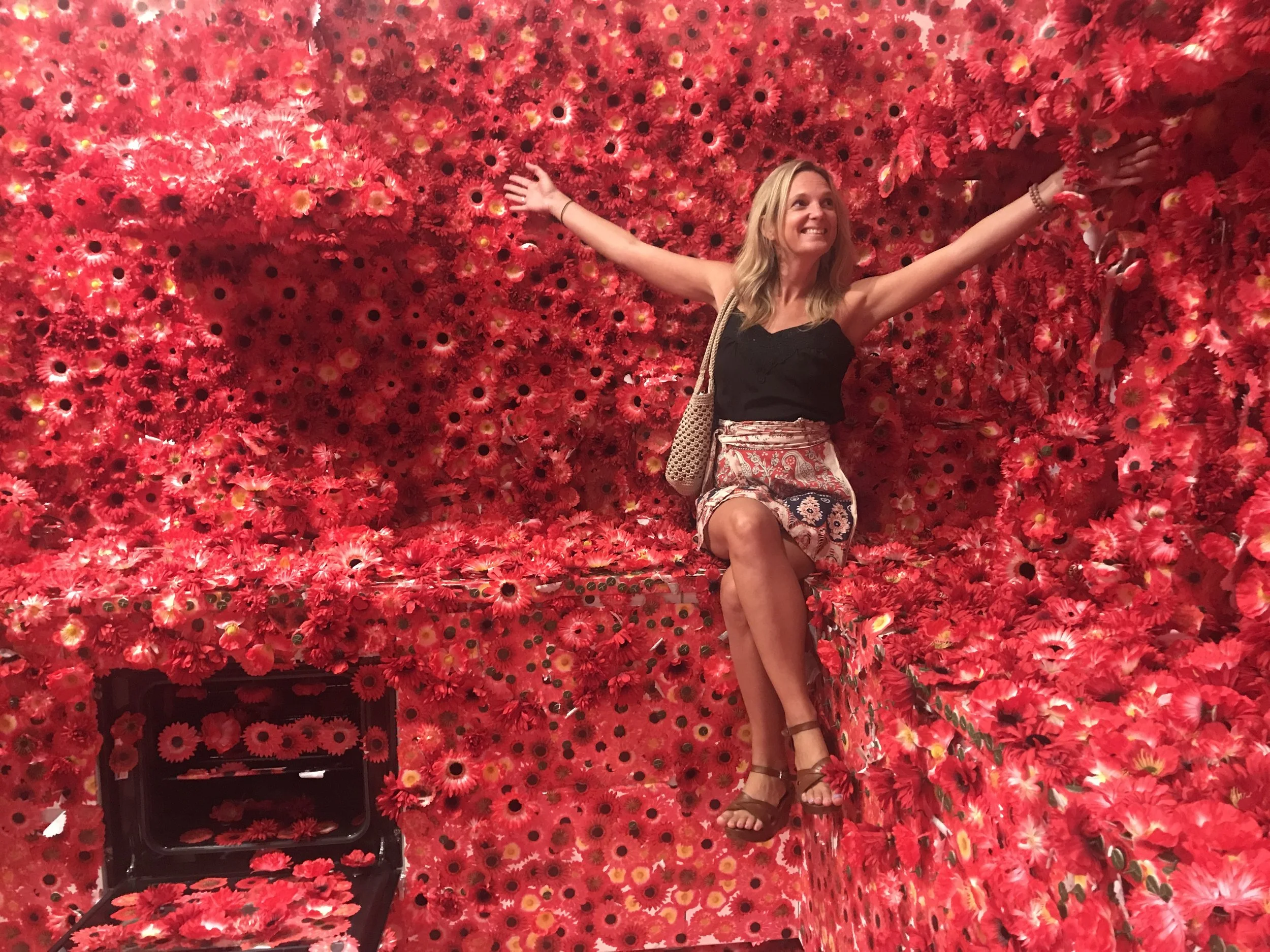 Multi-hyphenate artist Leesa Maree sitting in a sea of red flower at the NGV Yayoi Kusama exhibit, Melbourne.
