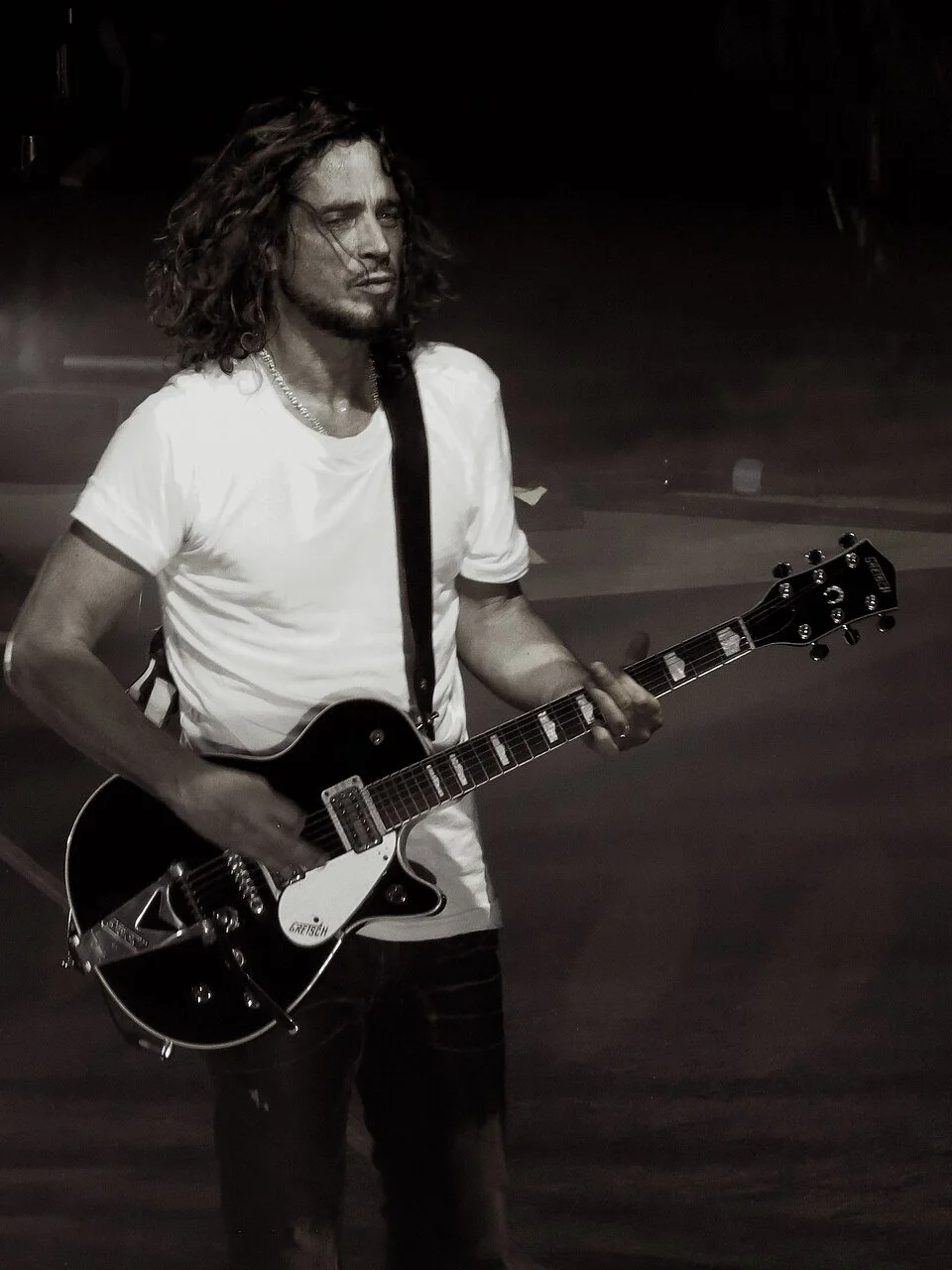 Chris Cornell on stage in white T-shirt with guitar.