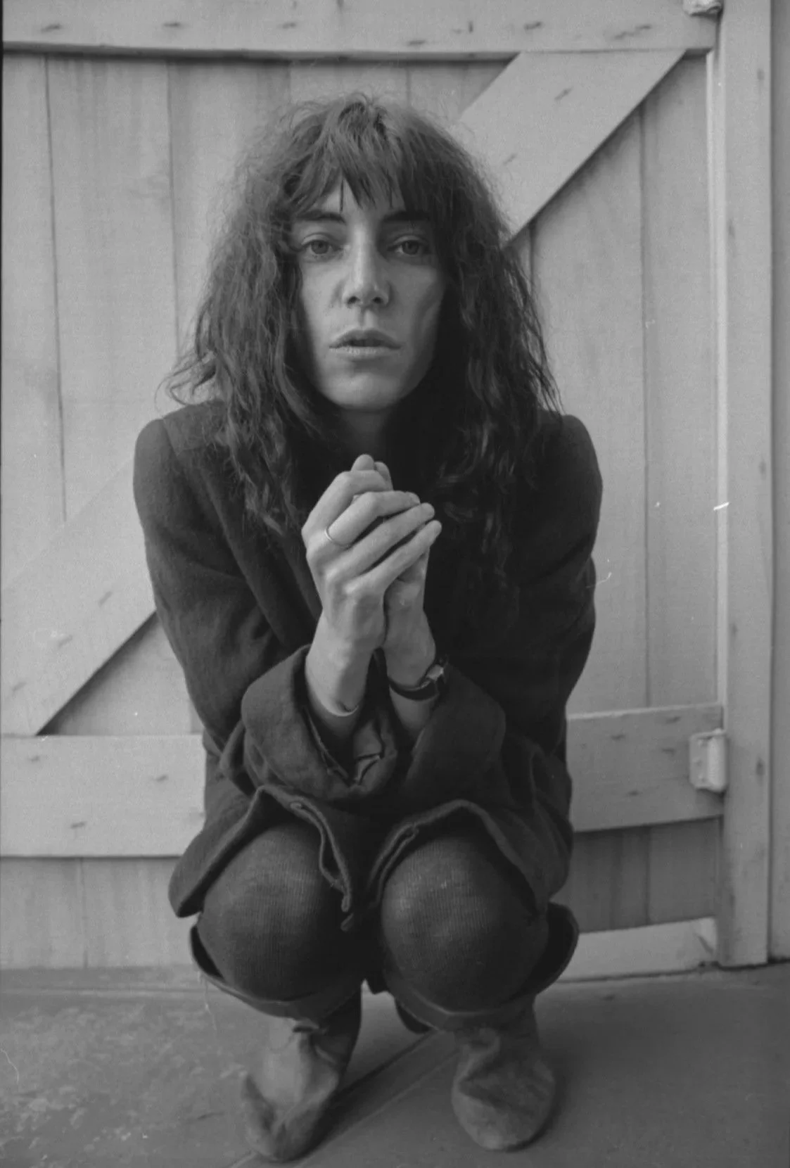 Patti Smith photograph taken in black and white of her crouched down and hands clasped at the heart.