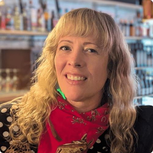 Lorna has long blonde hair. She is wearing a red neck scarf and smiling at the camera.