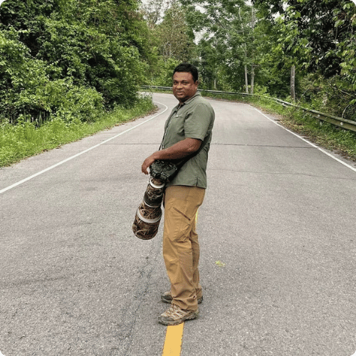 Charuka is standing on a road holding a large camera