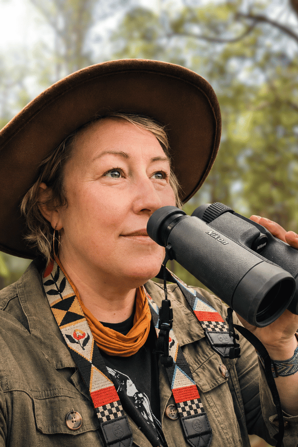 Kirsty is in the forest wearing a broadrimmed hat and holding a pair of binoculars