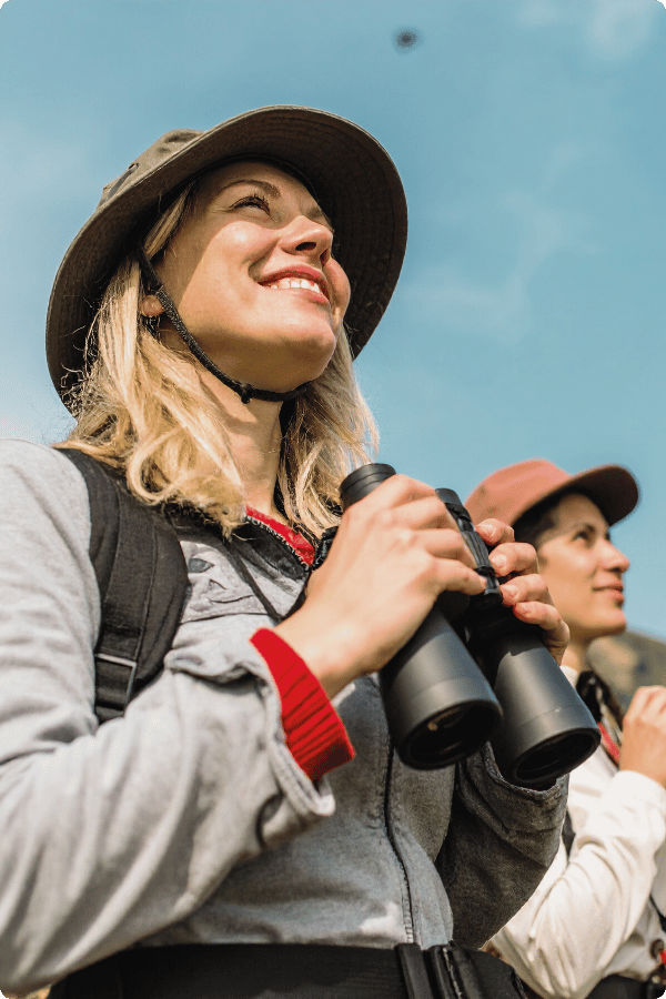 A woman is birdwatching. She is holding binoculars and looking up at the sky. She's in a group.