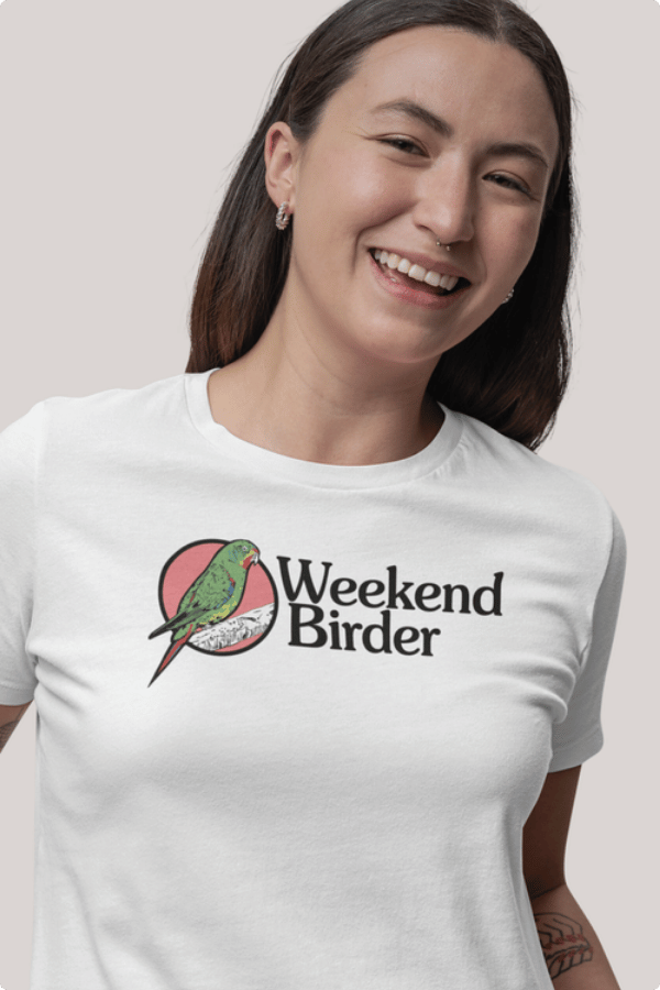 A woman wears a t-shirt that has an illustration of a Swift Parrot and text that says Weekend Birder