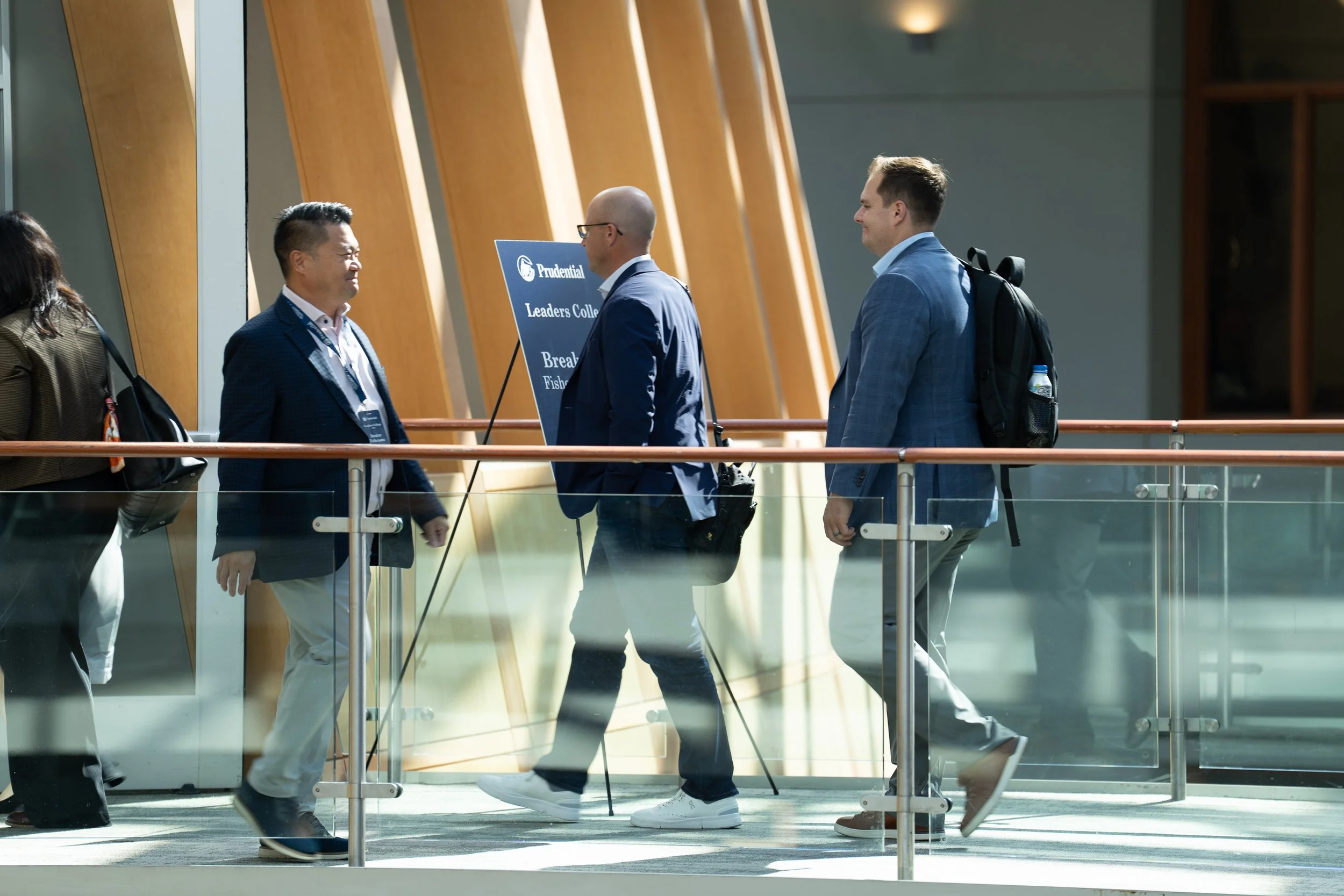Group of business professionals standing and talking inside a modern building with wooden architectural elements and large windows.