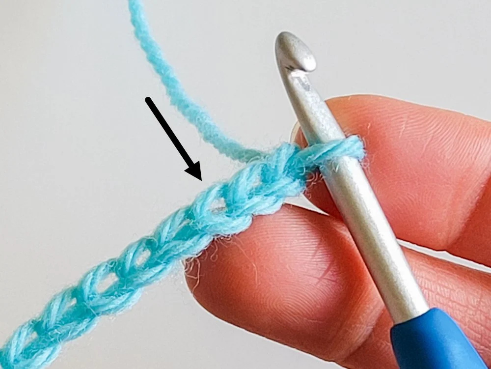 A chain crocheted with light blue yarn. A black arrow points to the third chain from the hook.