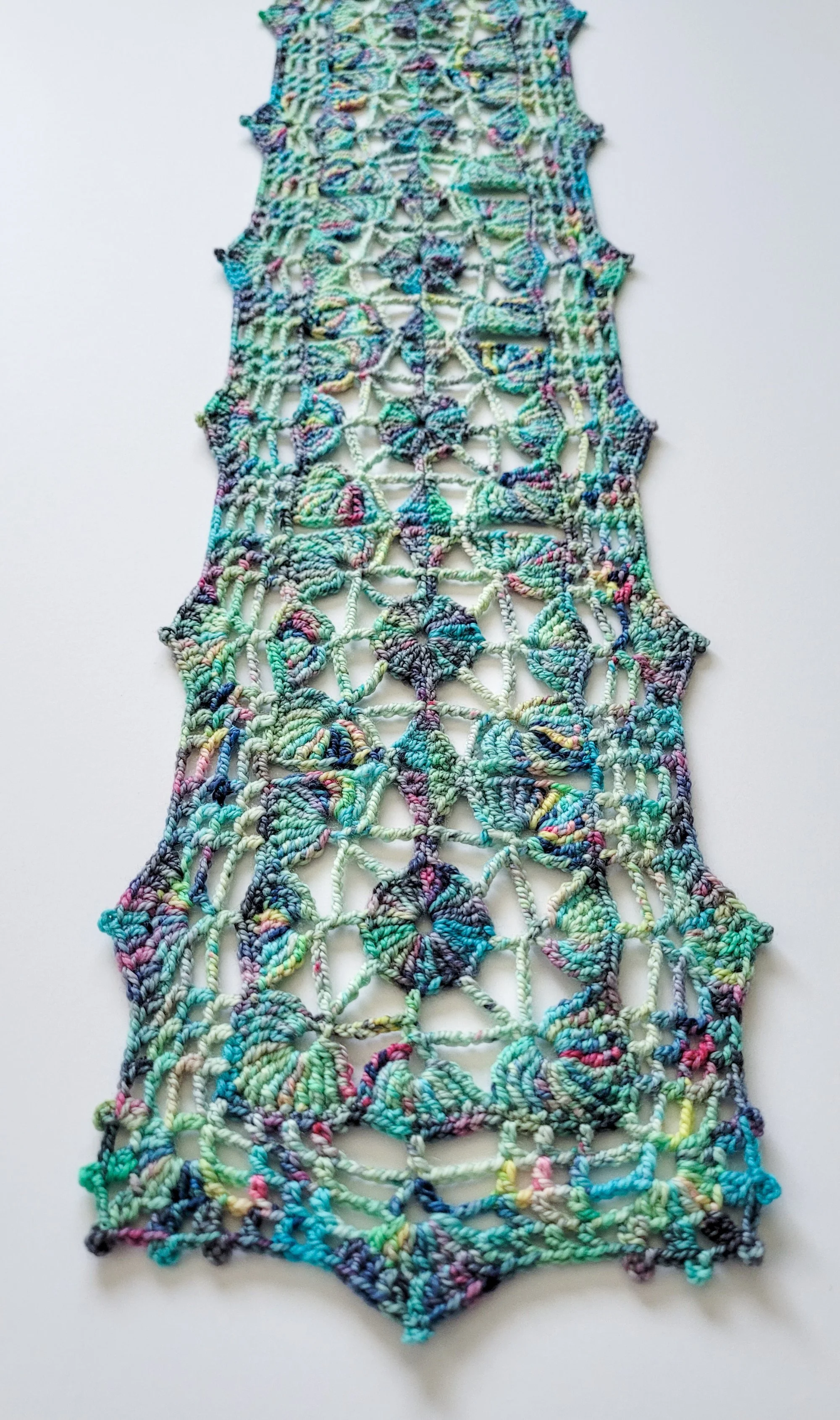 A lace scarf made with a variegated yarn in shades of blue, green, yellow, and purple.