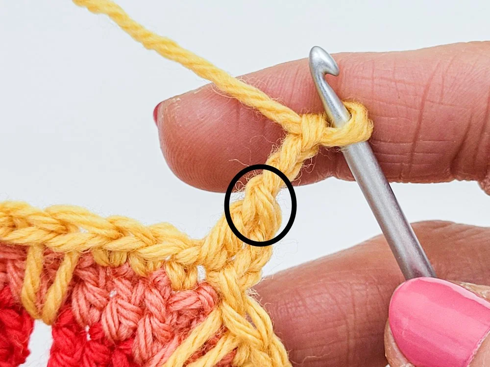 A double crochet and chain-3 worked in yellow yarn. A black circle is drawn around the top two front loops at the top of the double crochet stitch.