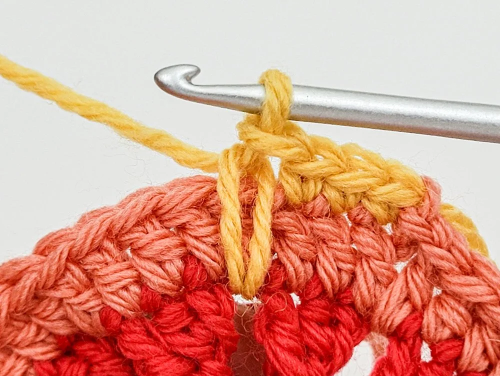 A completed spike single crochet worked into the space between red triangle petals 2 rounds below.