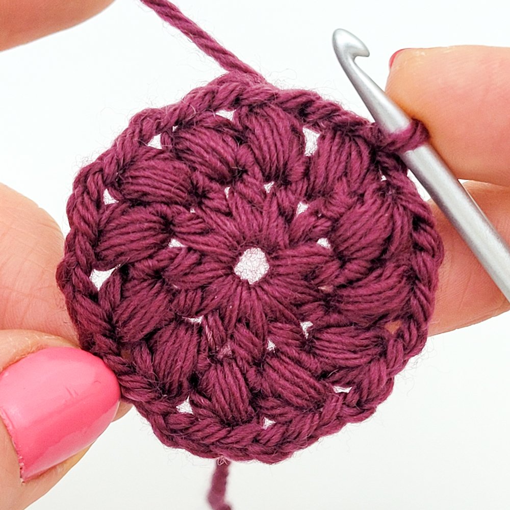 Rnd 2 complete. A crochet circle made with purple yarn and textured stitches.