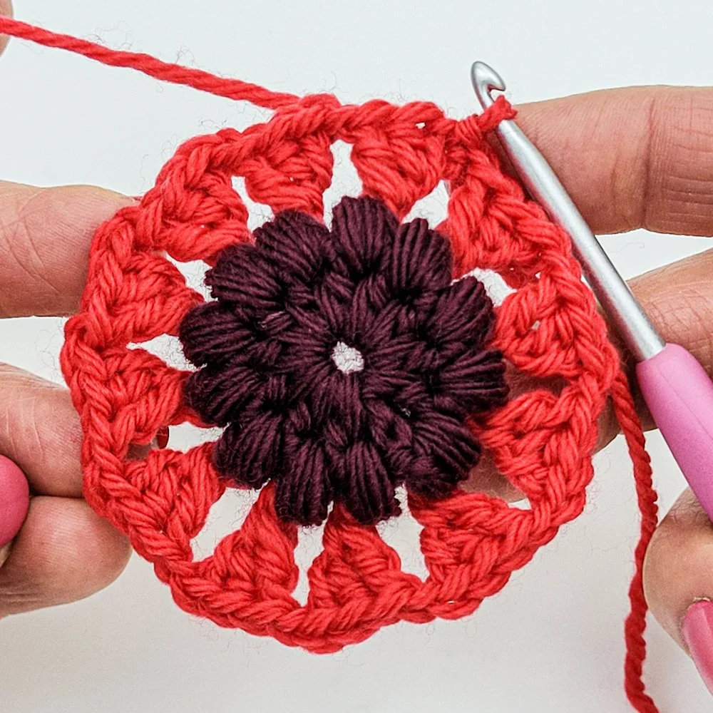 Rnd 4 complete. A crochet circle with red triangles radiating outward from a textured purple center.