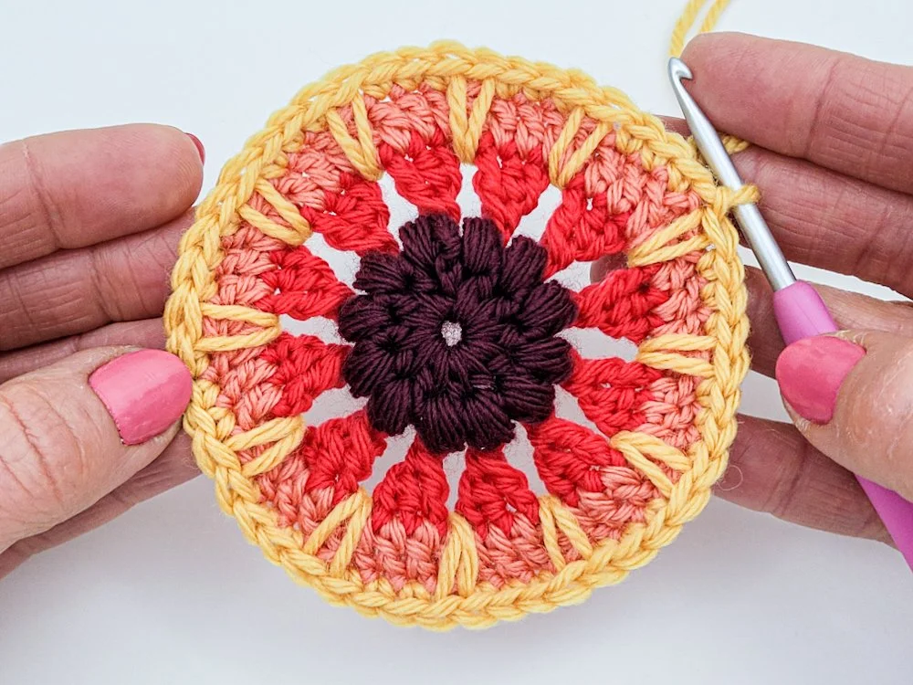 Rnd 6 complete. A textured crochet circle in purple, red, peach, and yellow.