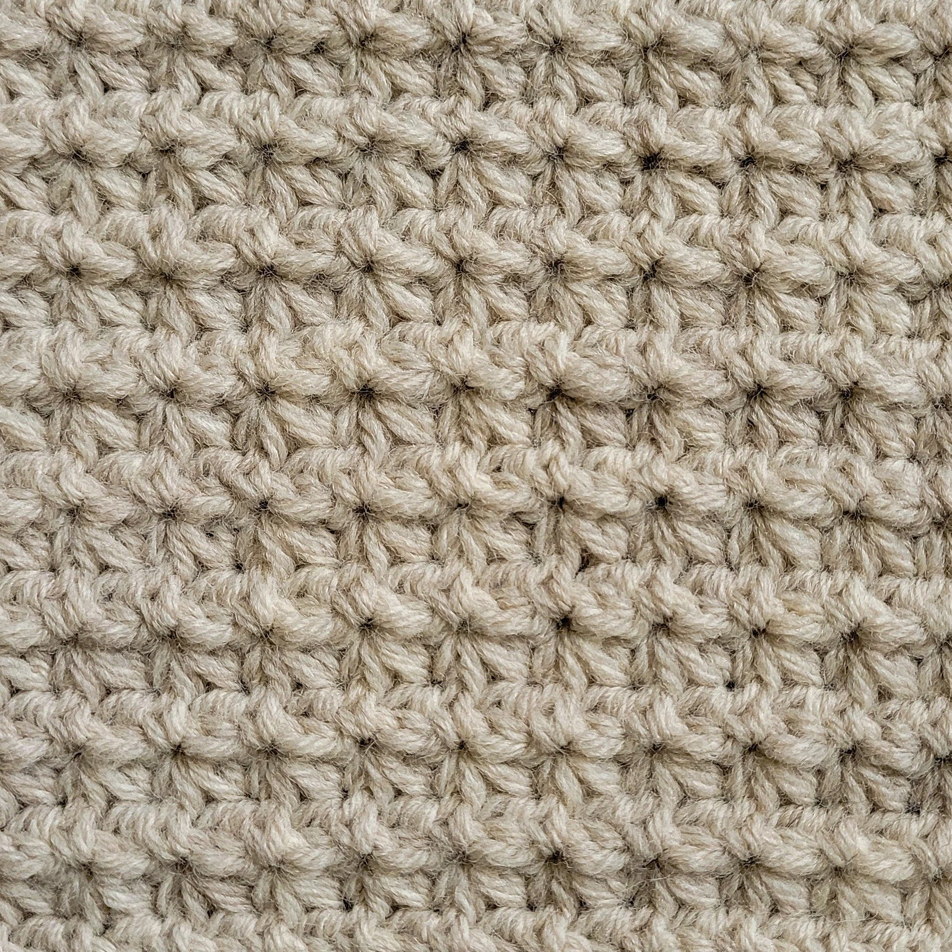 Closeup of a highly textured crochet stitch featuring star-like clusters worked in a light beige yarn.