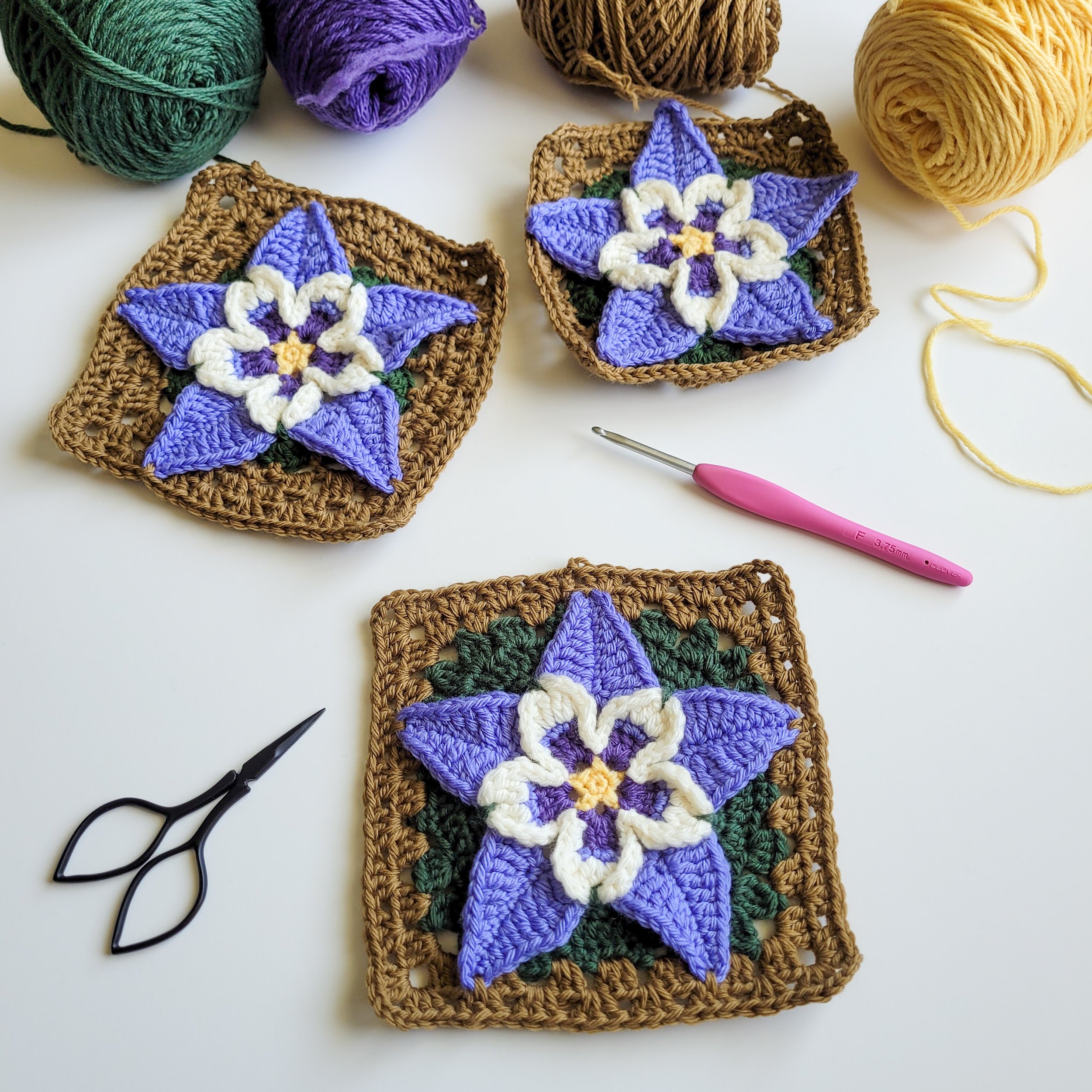 photo of 3 columbine motifs on a white table with a pair of scissors and a crochet hook