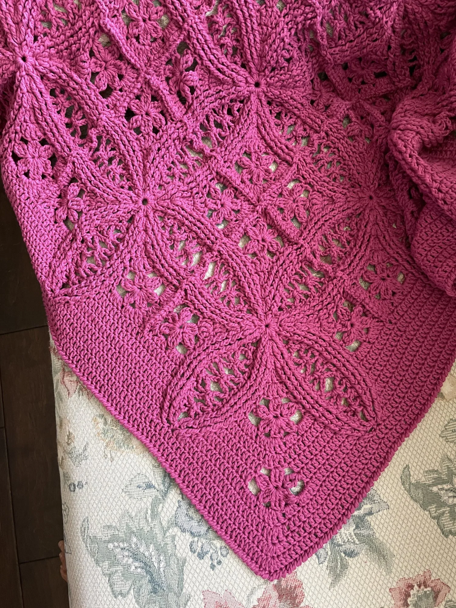 A Double Wedding Ring Blanket stitched in magenta yarn by tester Debbie Field is draped over the back of a chair.