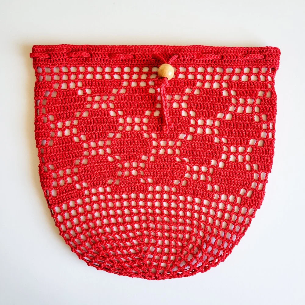 Red crocheted mesh bag with a drawstring and wooden bead closure. The bag has a polka dot design stitched in the side.