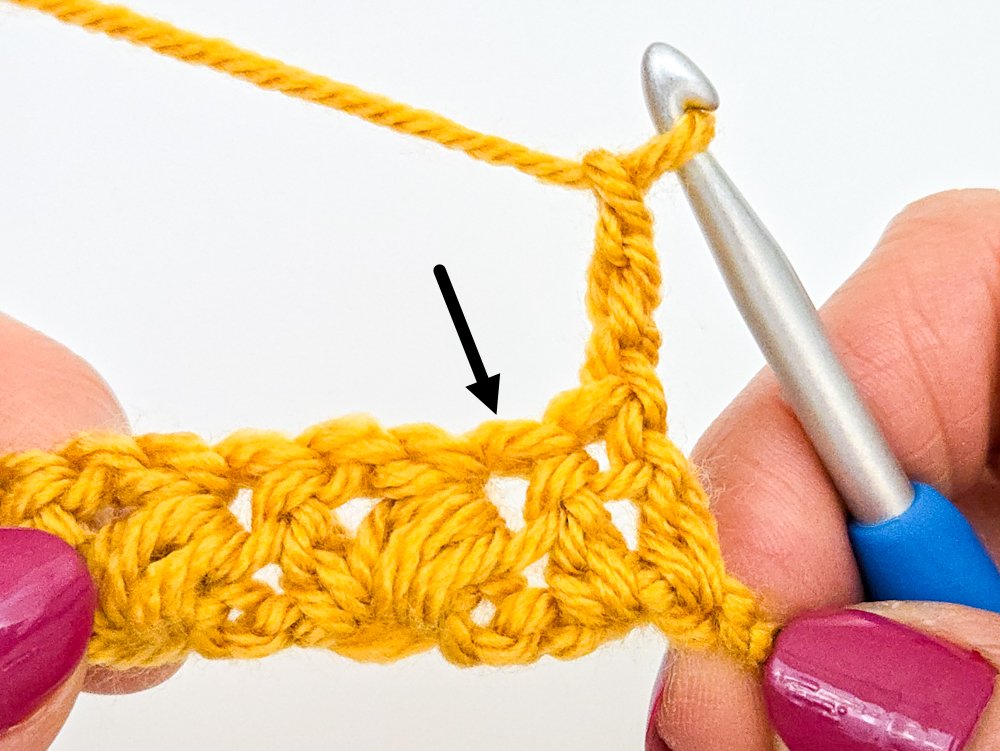 A black arrow points to the next double crochet in which you will work the first puff V-stitch of the row.