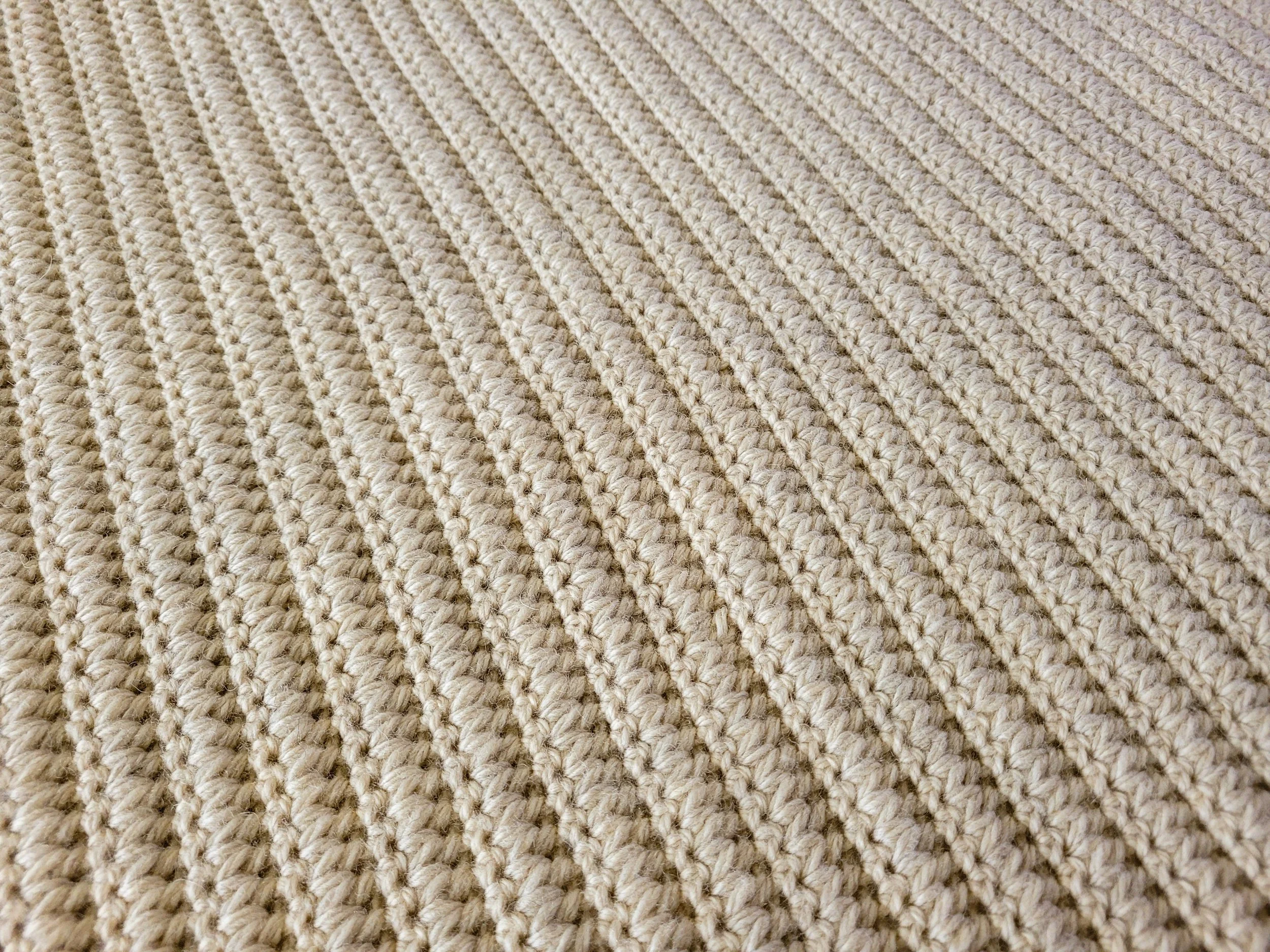 Close-up of a tan crochet blanket, showcasing the forked cluster stitch pattern that creates a highly textured and uniquely cozy fabric.