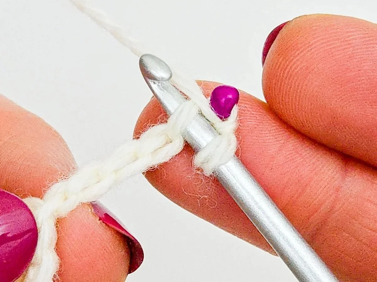 Hook inserted in back bar of second chain from hook. Working yarn has been moved to front, between hook and bead.