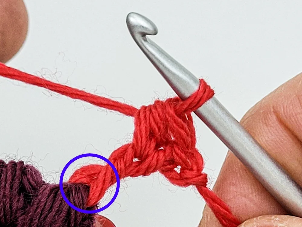 A half double crochet stitch worked into the side of a treble crochet using red yarn. A blue circle has been drawn around the bottom of the treble crochet stitch.
