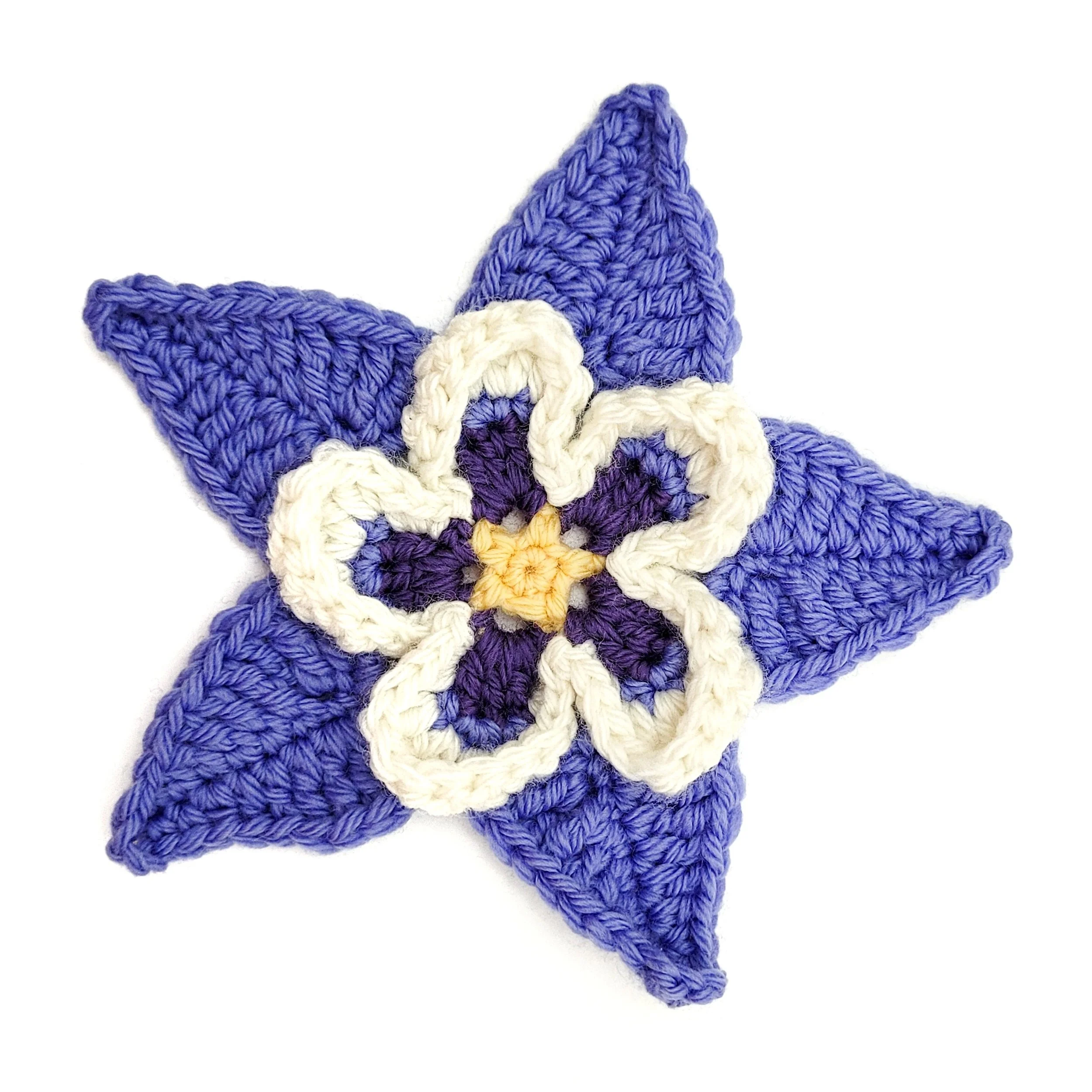 A crochet columbine flower made with periwinkle, purple, yellow, and white yarn.
