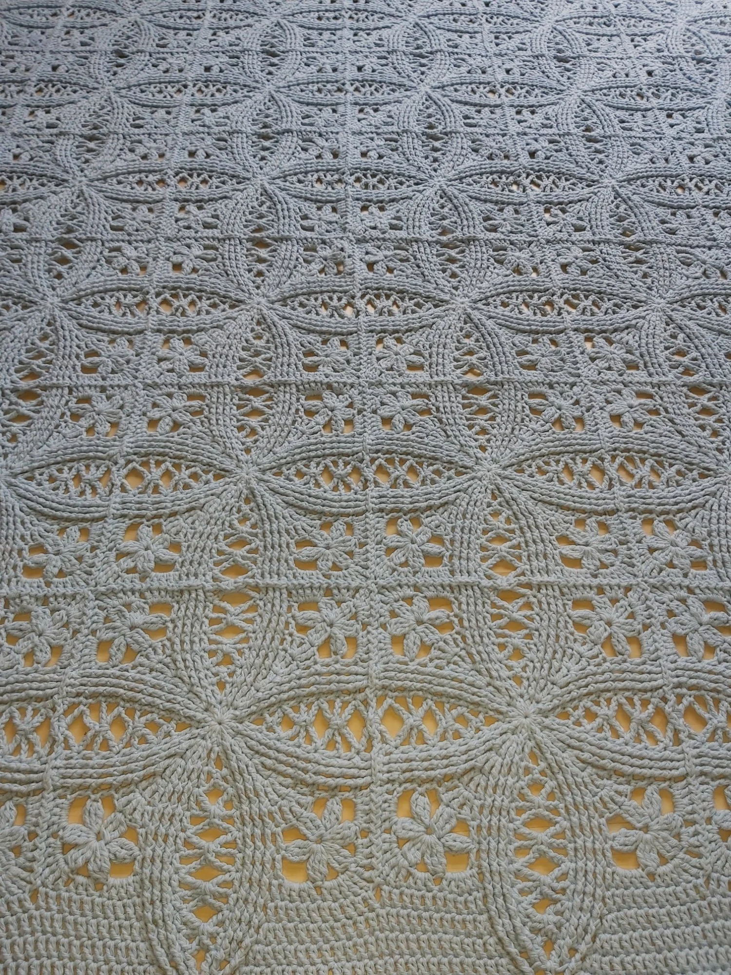 A Double Wedding Ring stitched with gray yarn by tester Odette Blaak is laid flat. Photographed at an angle, the dim light highlights the interlocking rings.