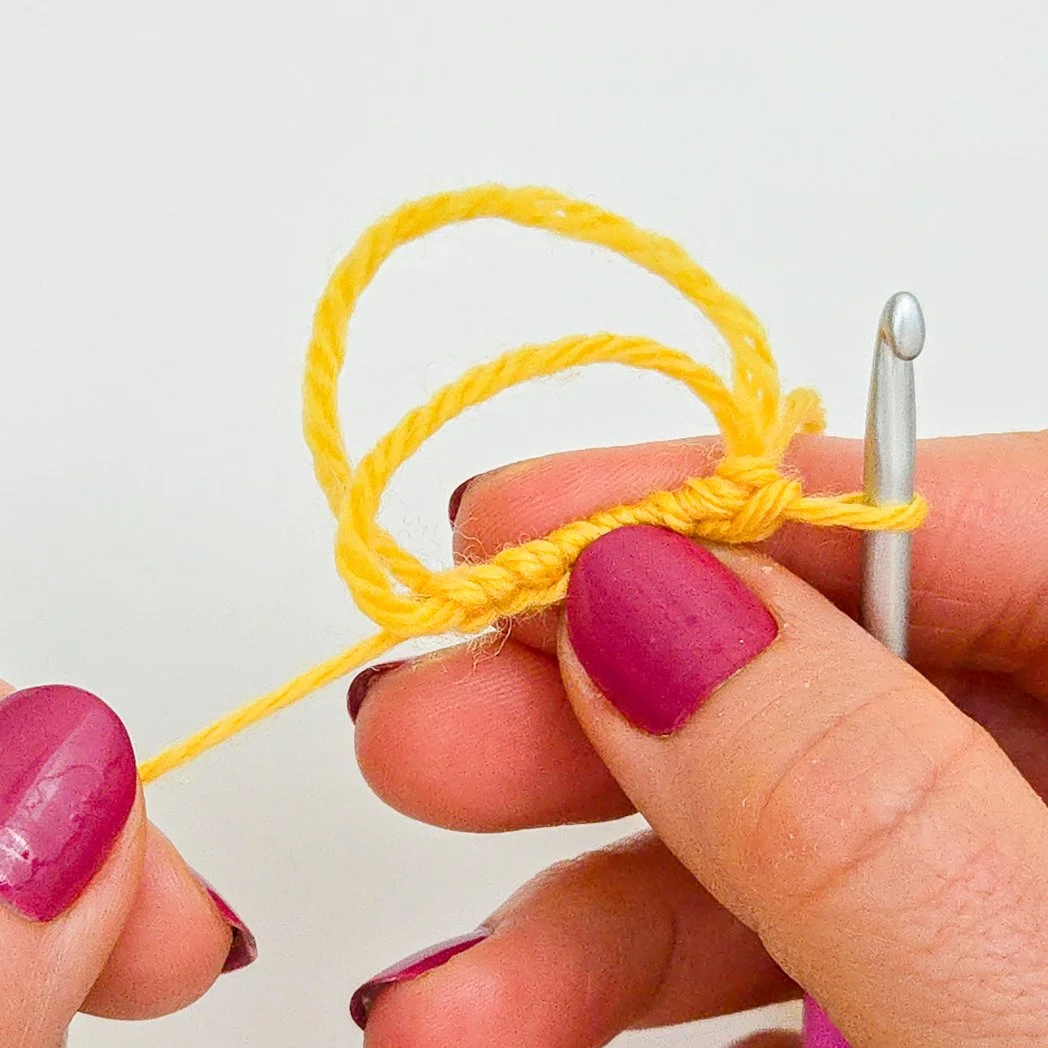Stitches of first round have been worked into the adjustable ring. Left hand is pulling tail end to begin closing loop.