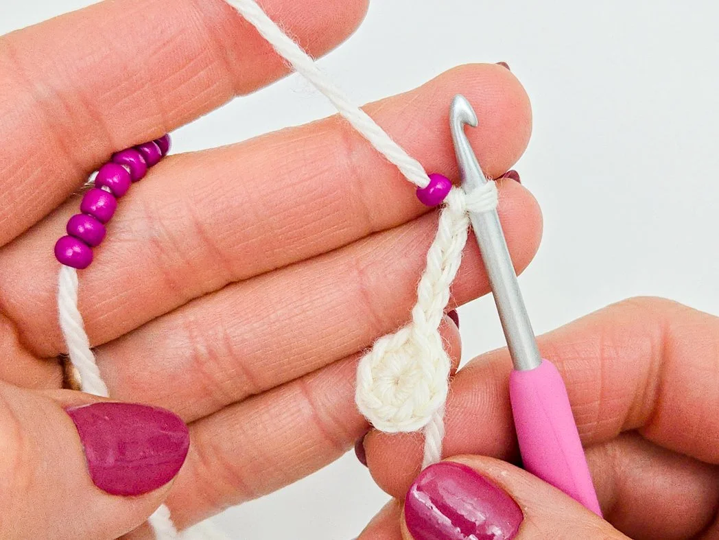 Chain 5 complete. A seed bead is positioned next to the crochet hook.