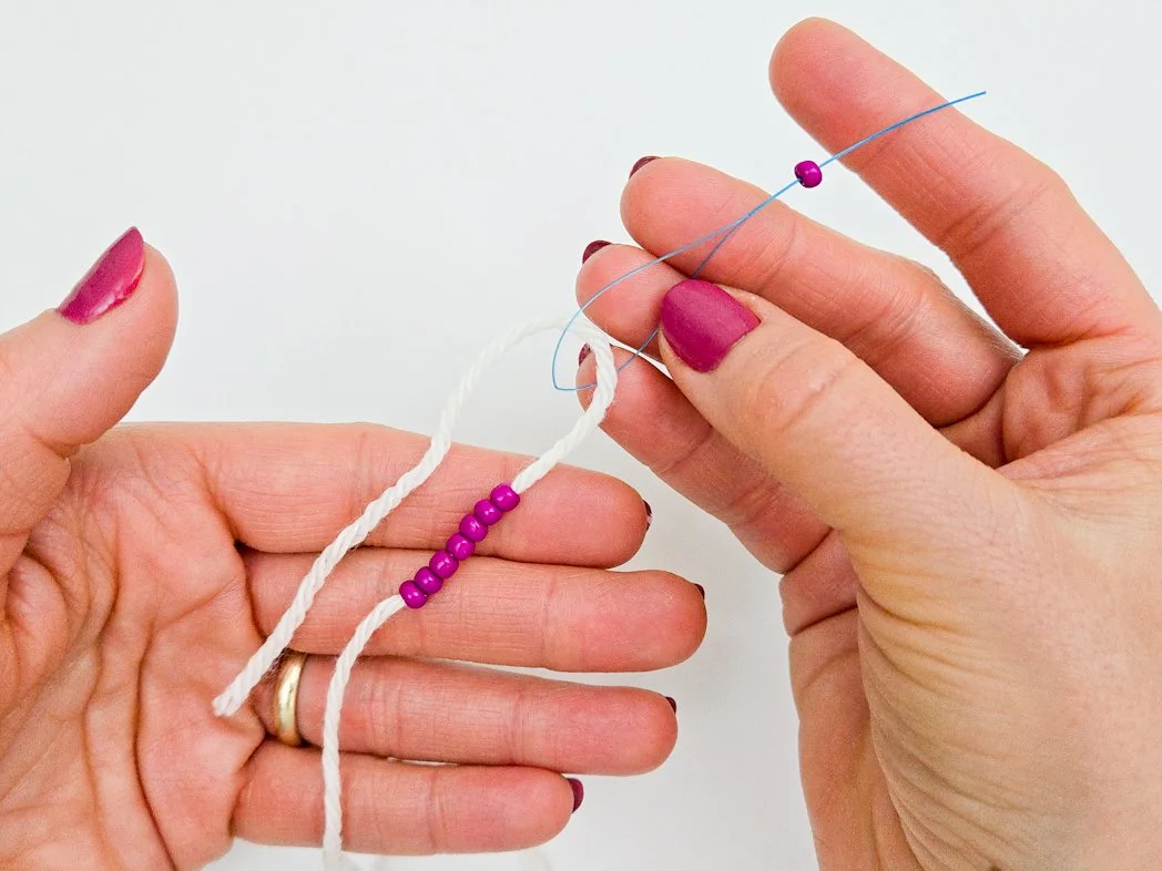 Eight pink round seed beads have been strung onto a white yarn, using a blue dental floss threader.