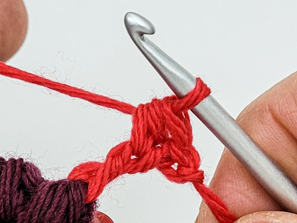 A half double crochet stitch worked into the side of a treble crochet using red yarn.