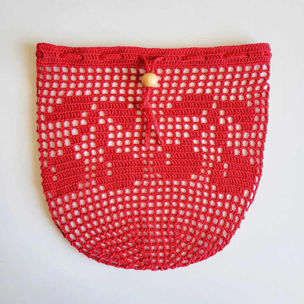 Red crocheted mesh bag with a drawstring and wooden bead closure. The bag has a cherries design stitched in the side.