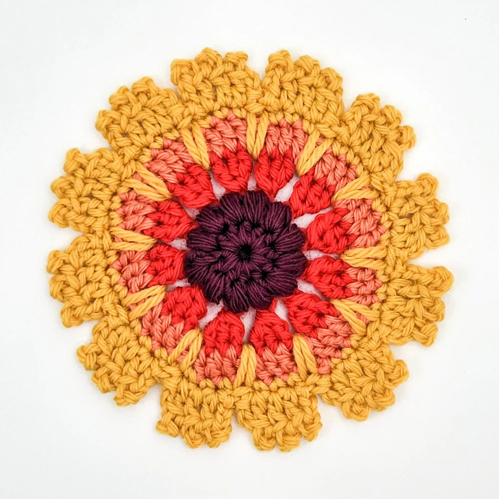 A crochet blanket flower made with red, coral, and yellow yarn on a white background.