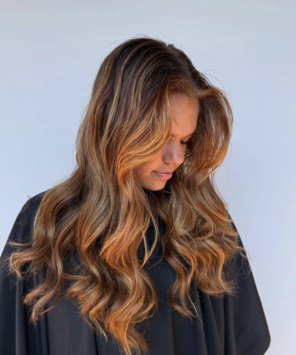 Woman with long wavy brown hair with highlights in a hair salon.