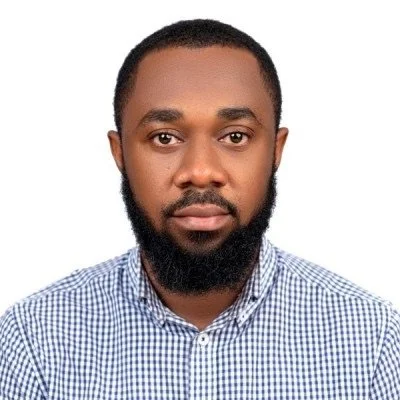 Headshot of a man with a beard wearing a blue and white checkered shirt against a plain white background.