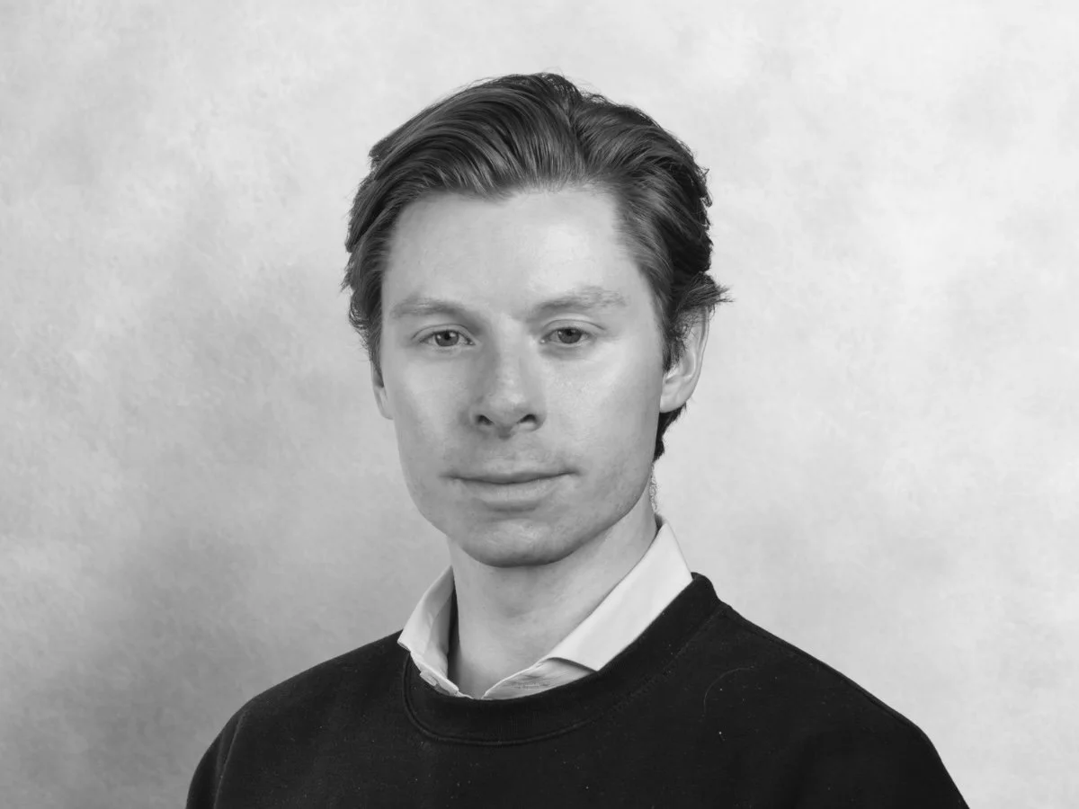 Black and white portrait of filmmaker, videographer and video production professional Kyle Edwardson, based out of New York City with neatly combed hair, wearing a collared shirt under a sweater, against a plain background.