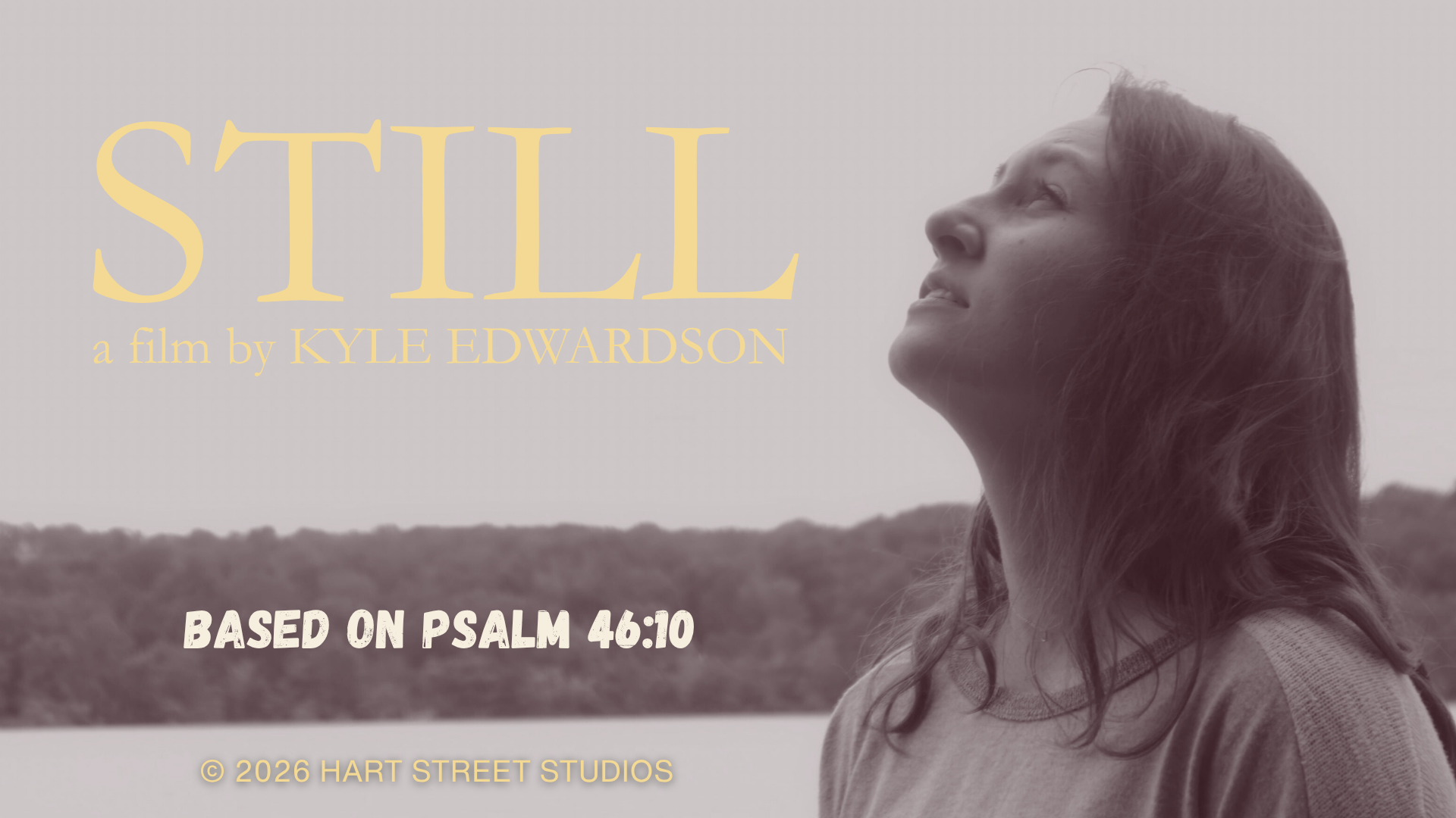 A woman with long hair looking up, standing outdoors near a body of water with a distant tree-lined shoreline, in black and white with text overlay about the film "Still" by Kyle Edwardson, based on Psalm 46:10.