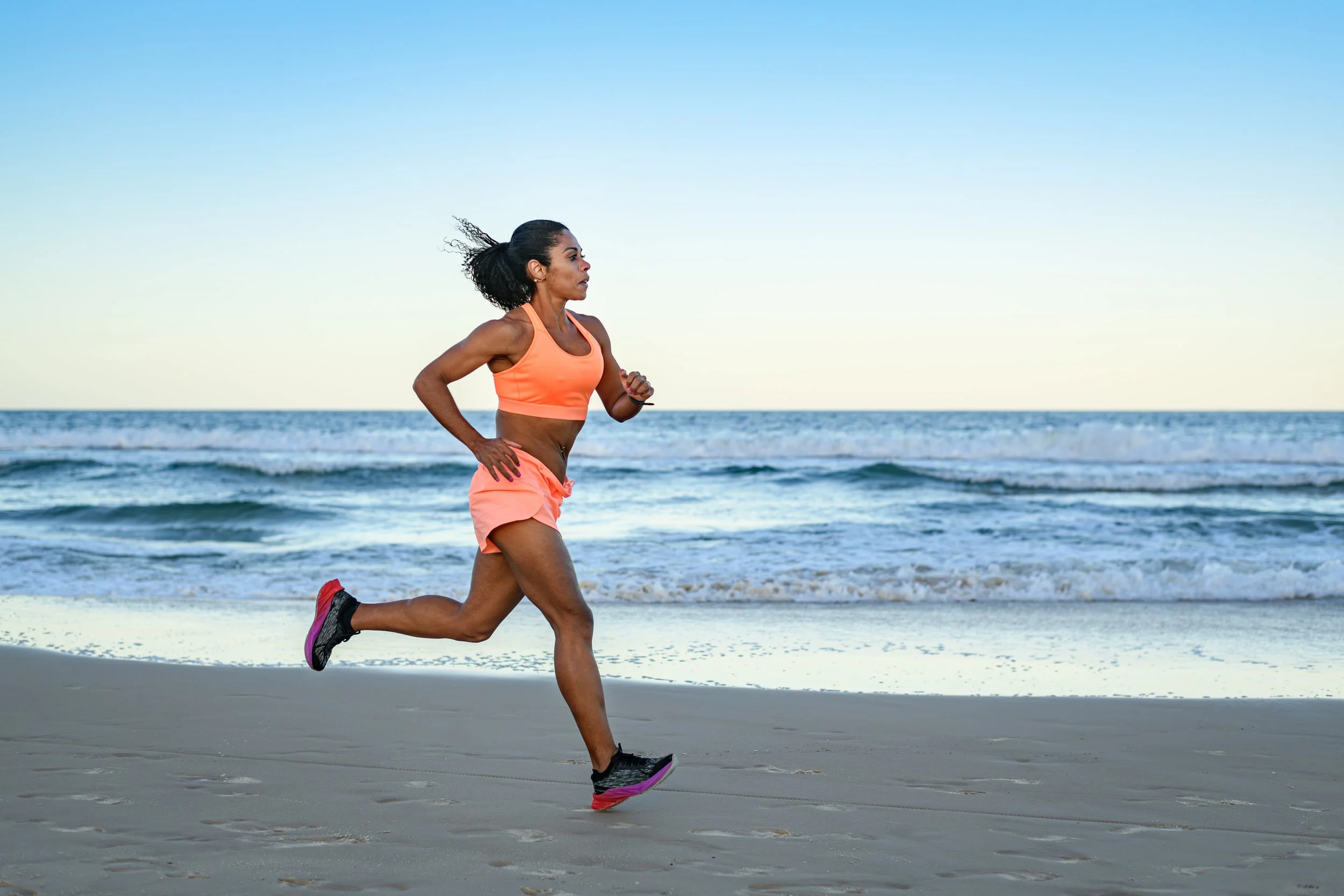 A woman running on the beach during sunrise or sunset with the ocean in the background.