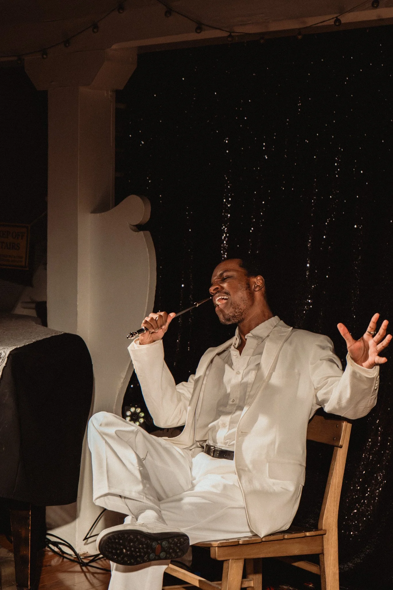A performer in a white suit sings from a wooden chair in Macbeth: A Musical Adaptation