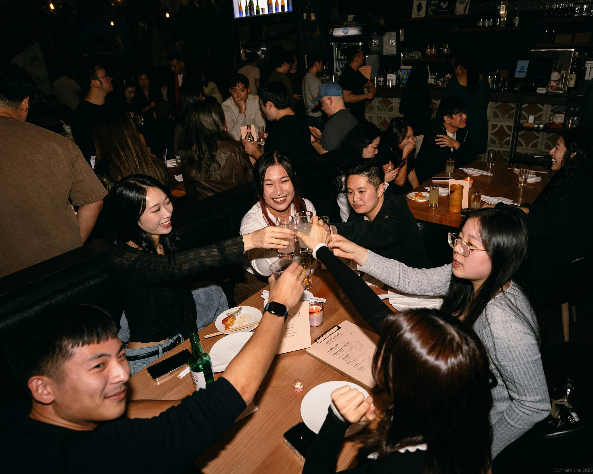 Group of friends at a restaurant clinking shot glasses and smiling.