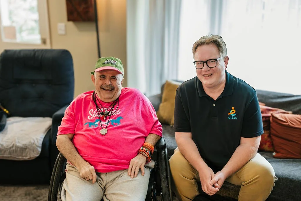 Don and his support Coordinator smiling. Don is wearing a bright pink shirt and his Support Coordinator is wearing a dark eitas shirt.