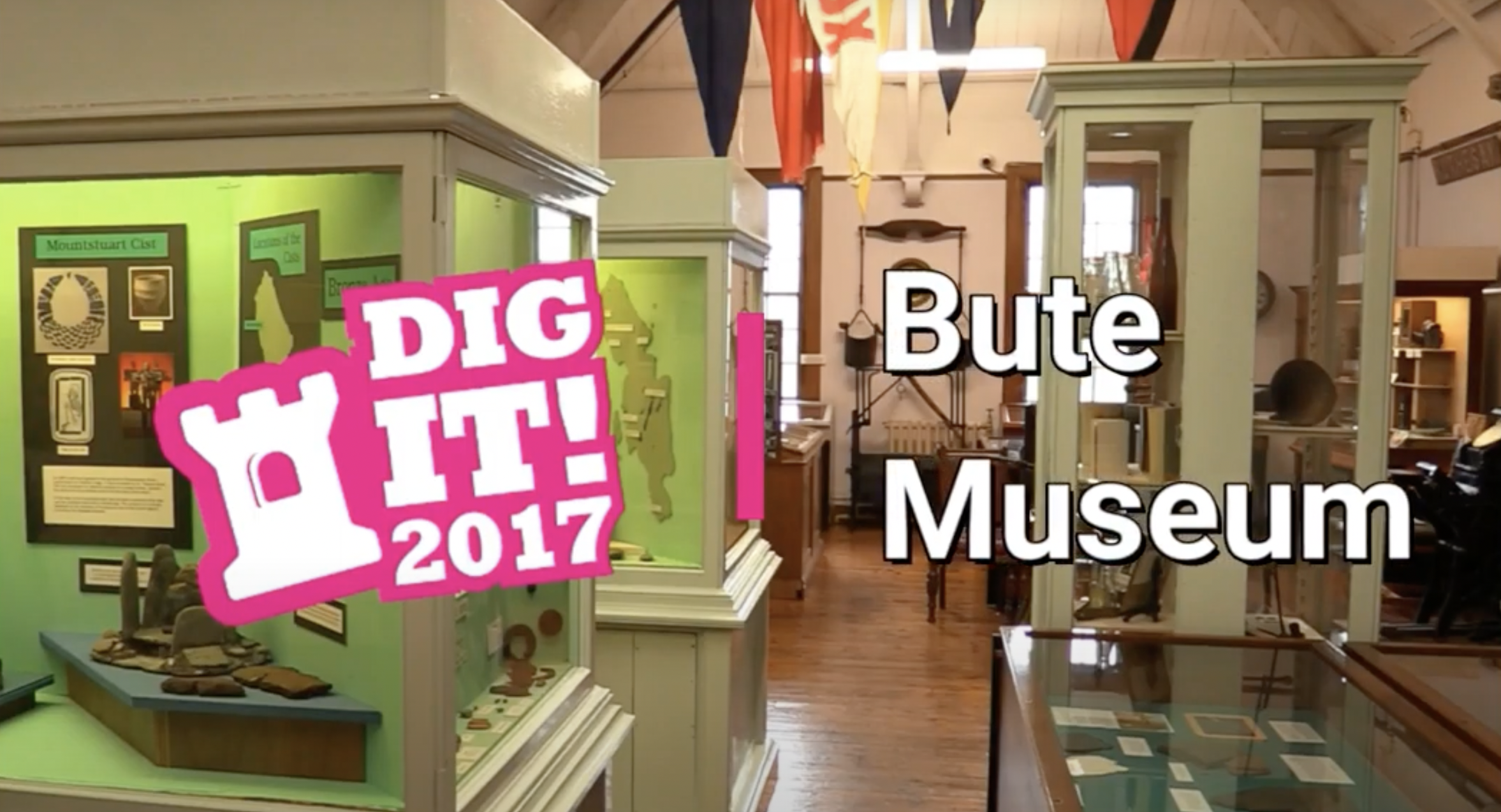 Inside the galleries of Bute Museum, with a green display case with ancient objects on the left. Graphics saying 'Dig It! 2017' and 'Bute Museum' are overlaid on it.