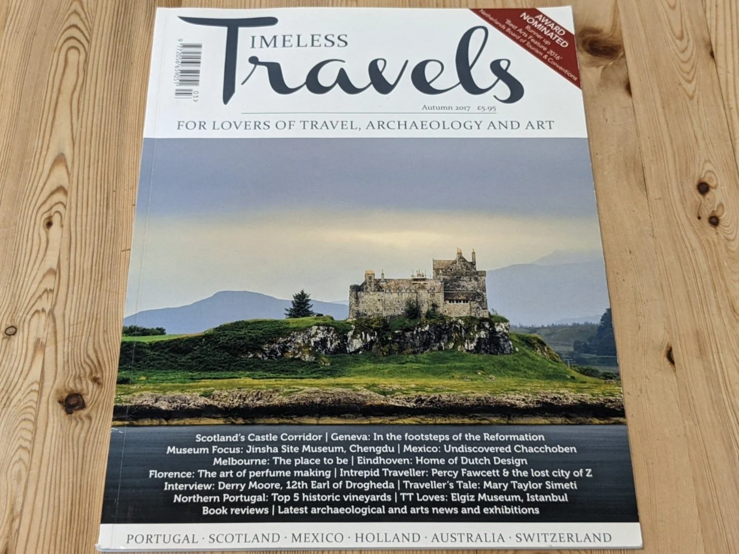 Cover of Timeless Travels magazine with a picture of Duart Castle perched atop a rocky outcrop overlooking a body of water and backed by high hills.