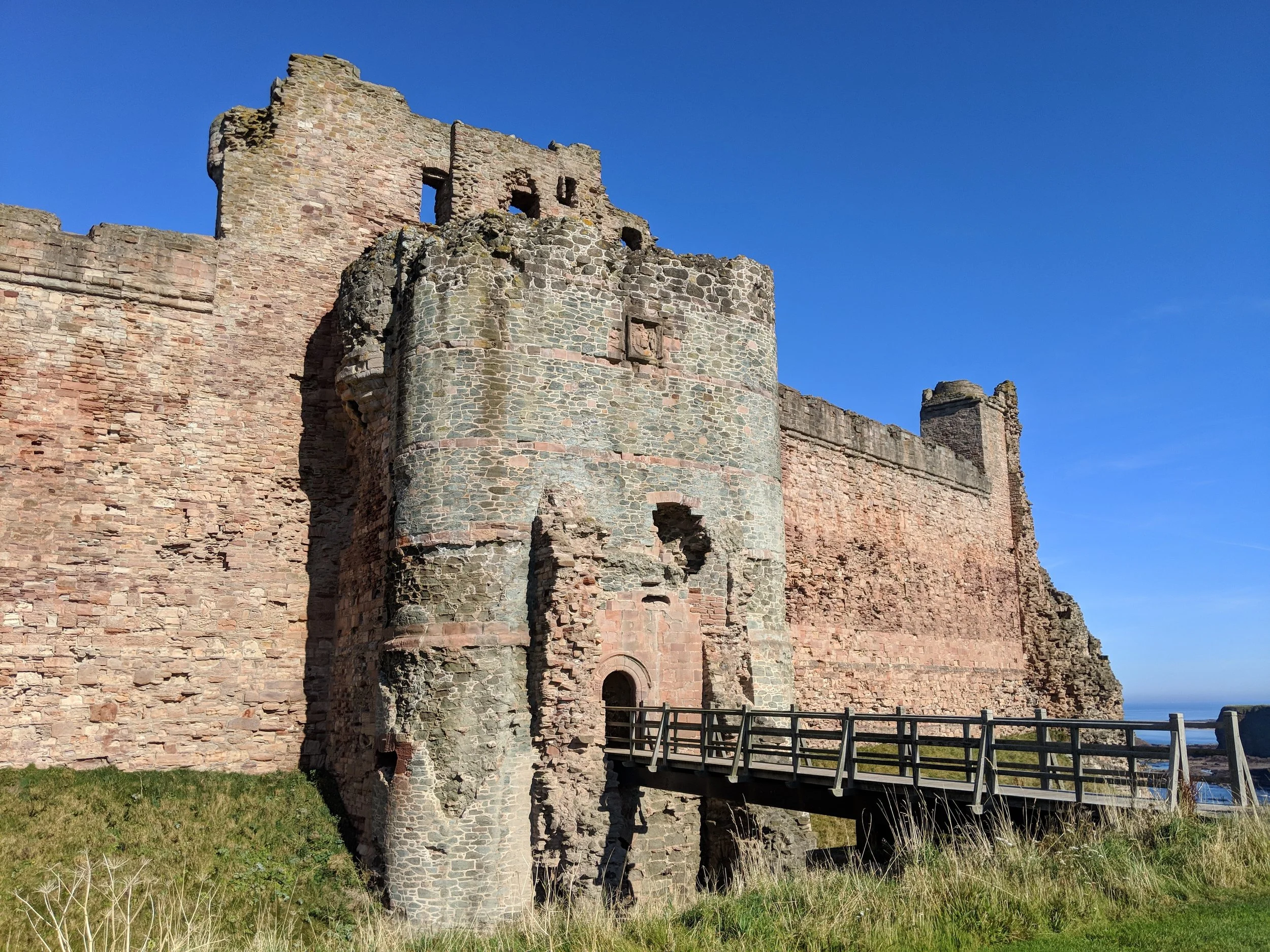 A huge red sandstone castle gatehouse with a drawbridge spanning a chasm. Bright blue skies overhead.
