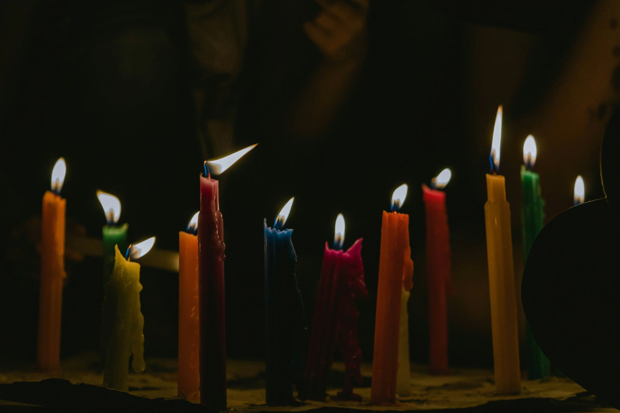 Multiple colorful birthday candles burning in a dark setting.